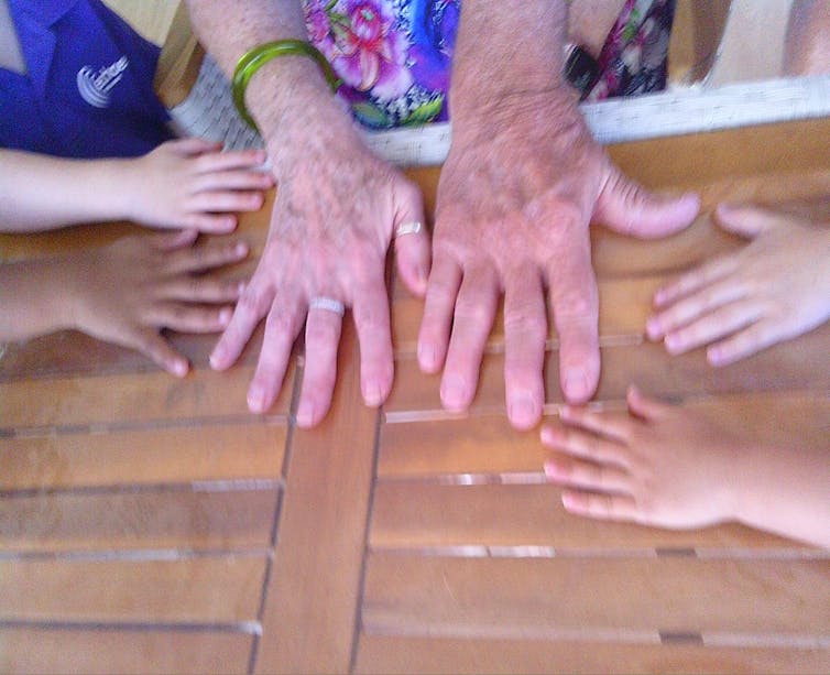 Children's hands on a table next to older adults' hands.